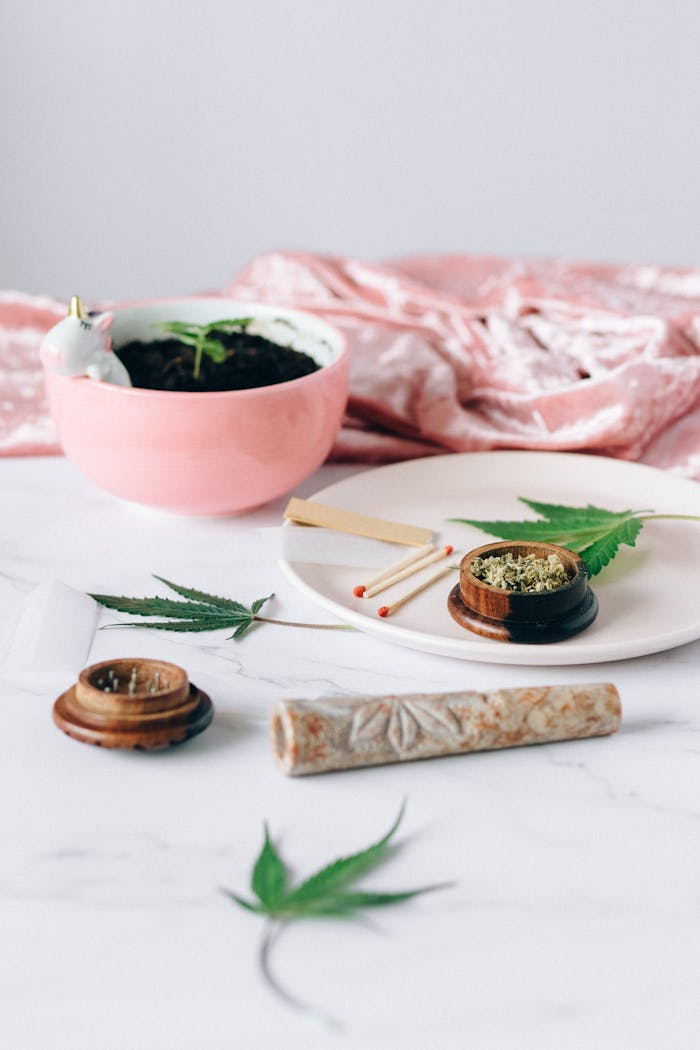 Marble surface with cannabis leaves, grinder, and pink planter creating a relaxed atmosphere.